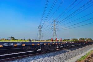 a series of flat-car trains speeding by against the backdrop of high-voltage power lines during a clear blue sky photo