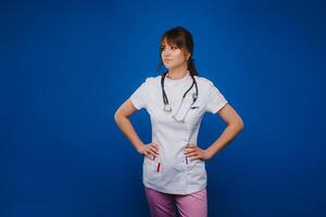 A female doctor, gesticulating, checks the heartbeat in the doctor's office at the hospital with a stethoscope isolated on a blue background photo
