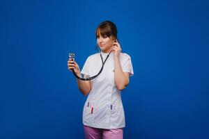 A female doctor, gesticulating, checks the heartbeat in the doctor's office at the hospital with a stethoscope isolated on a blue background photo