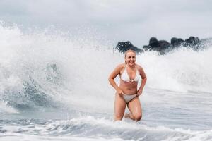 un niña con mojado pelo saltos terminado grande olas en el atlántico océano, alrededor un ola con salpicaduras de rociar y agua gotas.tenerife.españa foto