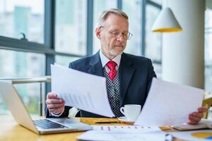 Thoughtful businessman is reading important business papers. Photo in front of the window with city view. Business process concept