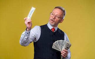 Happy elderly business man with fan of dollar bills isolated on yellow background. Seniour man guy won the lottery, lucky day. Human emotions and facial expressions photo