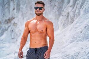 Fitness athlete in sunglasses posingoutdoor. Preparing for training in a quarry. Photoshoot in white mountains. Strong attractive bodybuilder. Lifestyle. White landscape. photo
