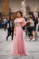 un joven hermosa novia soportes a el centrar de el antiguo ciudad de florencia en Italia. novia en un hermosa rosado vestir con un ramo de flores en toscana.italia foto