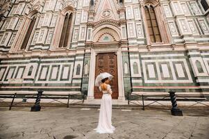 A beautiful stylish bride with an umbrella walks through the old city of Florence.Model with umbrellas in Italy.Tuscany. photo