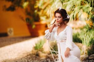 a beautiful bride is sitting on a chair and smiling in her underwear and dressing gown next to a Villa in Italy.morning of the bride in Tuscany photo