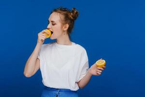 a young beautiful girl standing on a blue background holding lemons in her hand and biting. photo