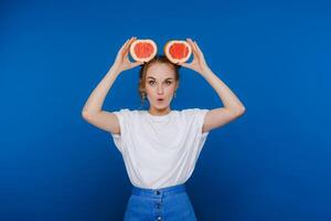 Surprised, the laughing girl holds the grapefruit like ears. Vegan lifestyle. Smiling woman , eating concept.Diet organic , weight loss and healthy food. Smoothies and fresh juice. photo