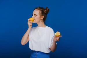 a young beautiful girl standing on a blue background holding lemons in her hand and biting. photo