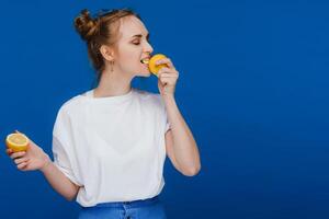 a young beautiful girl standing on a blue background holding lemons in her hand and biting. photo