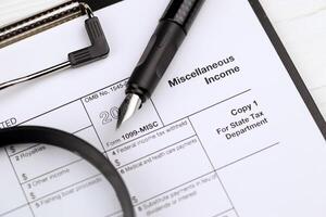 IRS Form 1099-misc Miscellaneous income blank on A4 tablet lies on office table with pen and magnifying glass photo
