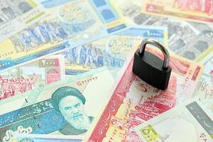 Small padlock lies on pile of iranian money. Sanctions, ban or embargo concept photo