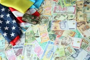 Toy tank on US flag and ukrainian flag on many banknotes of different currency photo