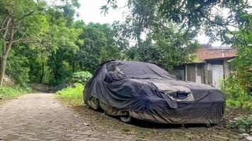 an old car covered in a cover abandoned on the side of the road near the forest photo