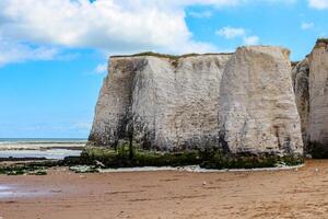 Majestic white cliffs against a blue sky with clouds, sandy beach in the foreground, and calm sea in the background in Margate, England. photo