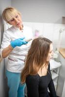 Professional beautician doing darsonval hair treatment procedure for young woman in beauty salon photo