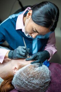 Procedure of eyebrow microblading. A master in black gloves is doing a blending needle of model's brow. photo