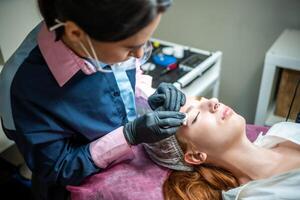 Procedure of eyebrow microblading. A master in black gloves is doing a blending needle of model's brow. photo