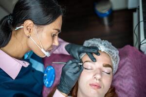 Procedure of eyebrow microblading. A master in black gloves is doing a blending needle of model's brow. photo