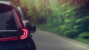 Rear side view of dark car with red light of brake. Driving speed on the aspahtl road with blurred of green forest beside road. photo