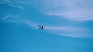 de Drönare flugor mot en bakgrund av blå himmel och moln, en se från Nedan. de quadcopter med de kamera svävar på en låg höjd över havet. snabbt roterande Drönare propellrar. video