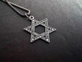 star of david silver pendant with diamonds laying on the dark gray fabric. photo