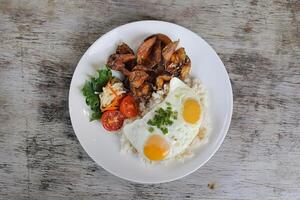 Fried Danggit with sunny egg and rice with tomato with salad served in dish isolated on wooden background top view of breakfast photo