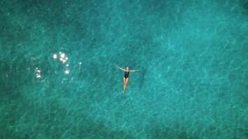 fêmea graciosamente flutuando em oceano superfície. aéreo Visão do uma pessoa espalhar braços relaxante dentro cristal Claro turquesa mar com Sol brilha. verão Férias. video