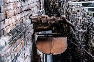 Metal sculpture. Half of lower human body sticks out of the wall. Bronze sculpture. Modern Art. Bare feet of a bronze sculpture inside the brick wall. Side view. photo