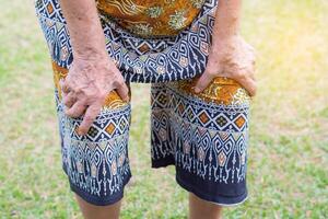 Senior woman suffering from knee pain in her garden. Knee pain may cause by muscle strain, tendinosis, ligament sprain, Arthritis pain concept photo