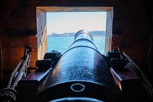 View out of a gunport in hull of the ship on the gun deck over the gun cannon muzzle in photo