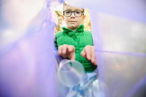 Environmental conservation concept.Little boy collects garbage and plastic bottles in the street to throw them in the trash bin photo