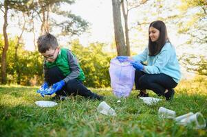 mujer voluntario y pequeño chico cosecha arriba el el plastico basura y poniendo eso en biodegradable bolsa de basura al aire libre. ecología, reciclaje y proteccion de naturaleza concepto. ambiental proteccion. foto