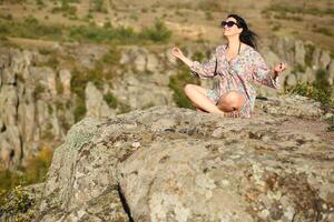 Young 35 year old caucasian woman in floral dress meditating on the edge of Aktove Canyon cliff, Ukraine photo