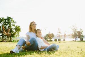 contento y simpático familia en naturaleza. emocional y joven madre abrazos su sonriente pequeño hija acostado en el césped. verano parque. positivo emociones.infancia. verano.estilo de vida foto