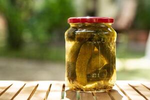 Salted, pickled cucumbers in a jar on a wooden table in the garden. Preservation, conservation. Background, copy space. Sunny bright day. photo