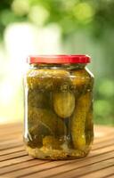 Salted, pickled cucumbers in a jar on a wooden table in the garden. Preservation, conservation. Background, copy space. Sunny bright day. photo