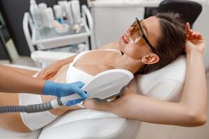 Female client in eyeglasses during armpit photo epilation procedure with ipl machine in beauty salon