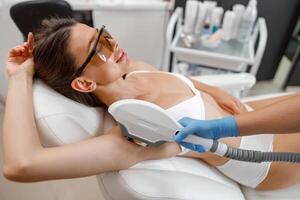 Female client in eyeglasses during armpit photo epilation procedure with ipl machine in beauty salon