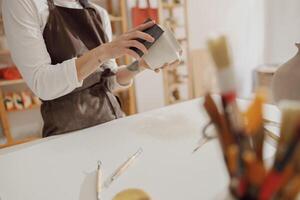 Close up of young female ceramist wearing apron work with unfired clay vase in pottery studio photo