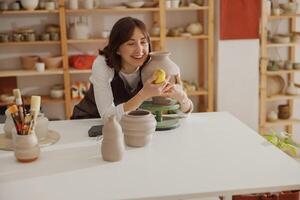 Professional potter wearing apron holding unfired clay vase while standing in pottery studio photo