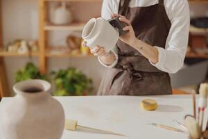 Close up of female ceramist wearing apron work with unfired clay vase in pottery studio photo