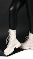 vrouw in zwart leer leggings draagt wit middellang laarzen met trekker zolen. model- poseren in studio. verticaal video