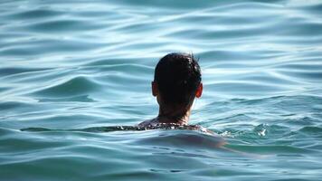 Woman swimming in calm sea at sunset, slow-motion, back view. Concept of body image and fitness, enjoying a serene beach. Happy woman with perfect fit body enjoys sea beach video