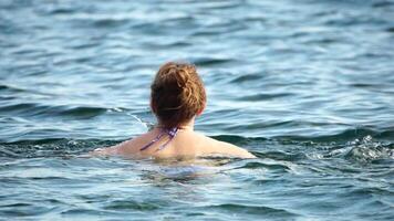 Woman swimming in calm sea at sunset, slow-motion, back view. Concept of body image and fitness, enjoying a serene beach. Happy woman with perfect fit body enjoys sea beach video