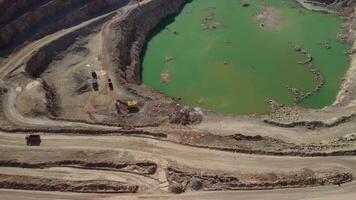 Aerial view of industrial opencast mining quarry with lots of machinery at work - extracting fluxes for the metal industry. Oval mining industrial crater, acid mine drainage in rock. video