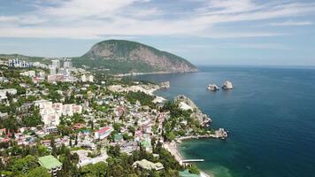 aereo panoramico Visualizza su gurzuf ricorrere città e orso montagna, ayu-dag, yalta, Crimea. primavera soleggiato giorno. natura estate oceano mare spiaggia sfondo. vacanza, viaggio e vacanza concetto. video