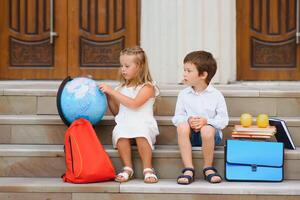 Two pupils of primary school. Boy and girl with school bags behind the back. Beginning of school lessons. Warm day of fall. Back to school. Little first graders. photo