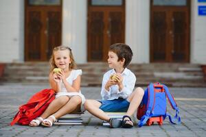 Two pupils of primary school. Boy and girl with school bags behind the back. Beginning of school lessons. Warm day of fall. Back to school. Little first graders. photo