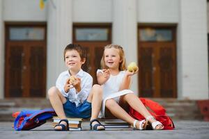 Two pupils of primary school. Boy and girl with school bags behind the back. Beginning of school lessons. Warm day of fall. Back to school. Little first graders. photo